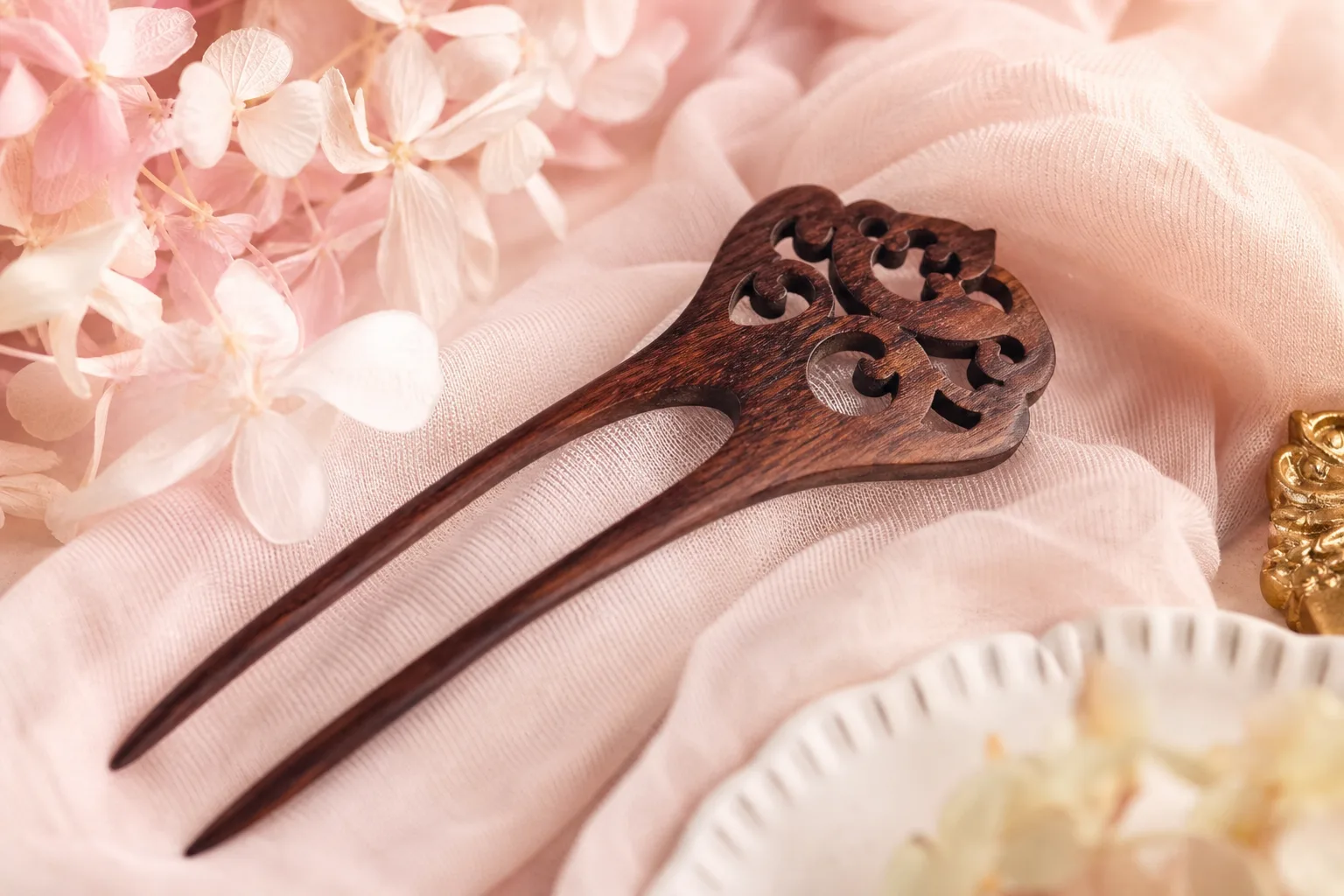Peigne à cheveux vintage en bois sculpté posé près d’une barrette ancienne et de fleurs séchées.