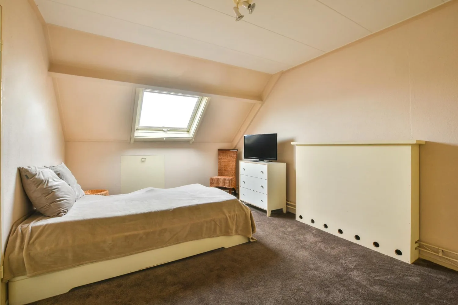 Chambre sous combles basse et lumineuse avec lit bas, rangements sur mesure sous pente et fenêtre de toit.
