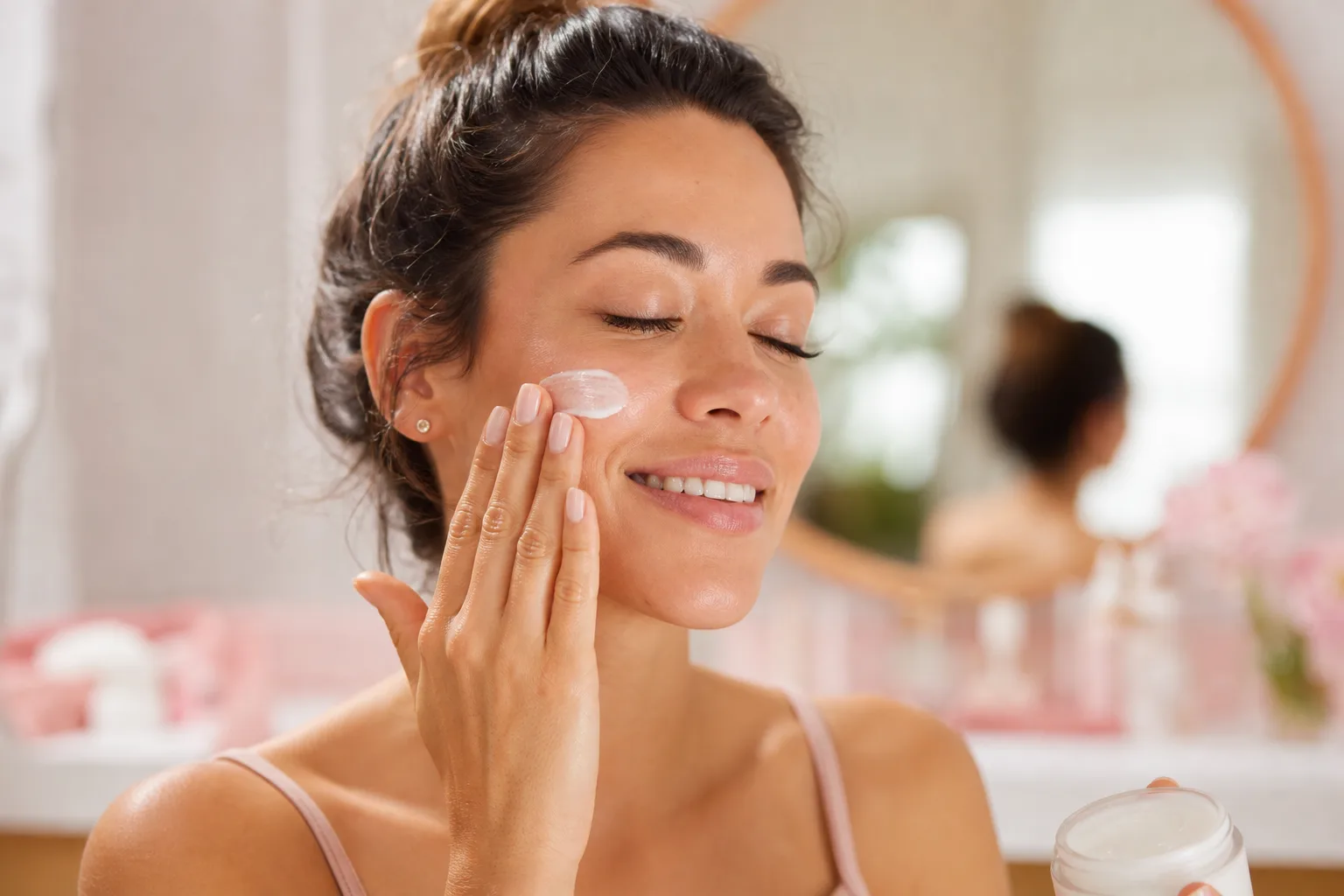 Femme appliquant délicatement une crème solaire invisible sur sa joue devant un miroir, pour un fini uniforme sans traces blanches.