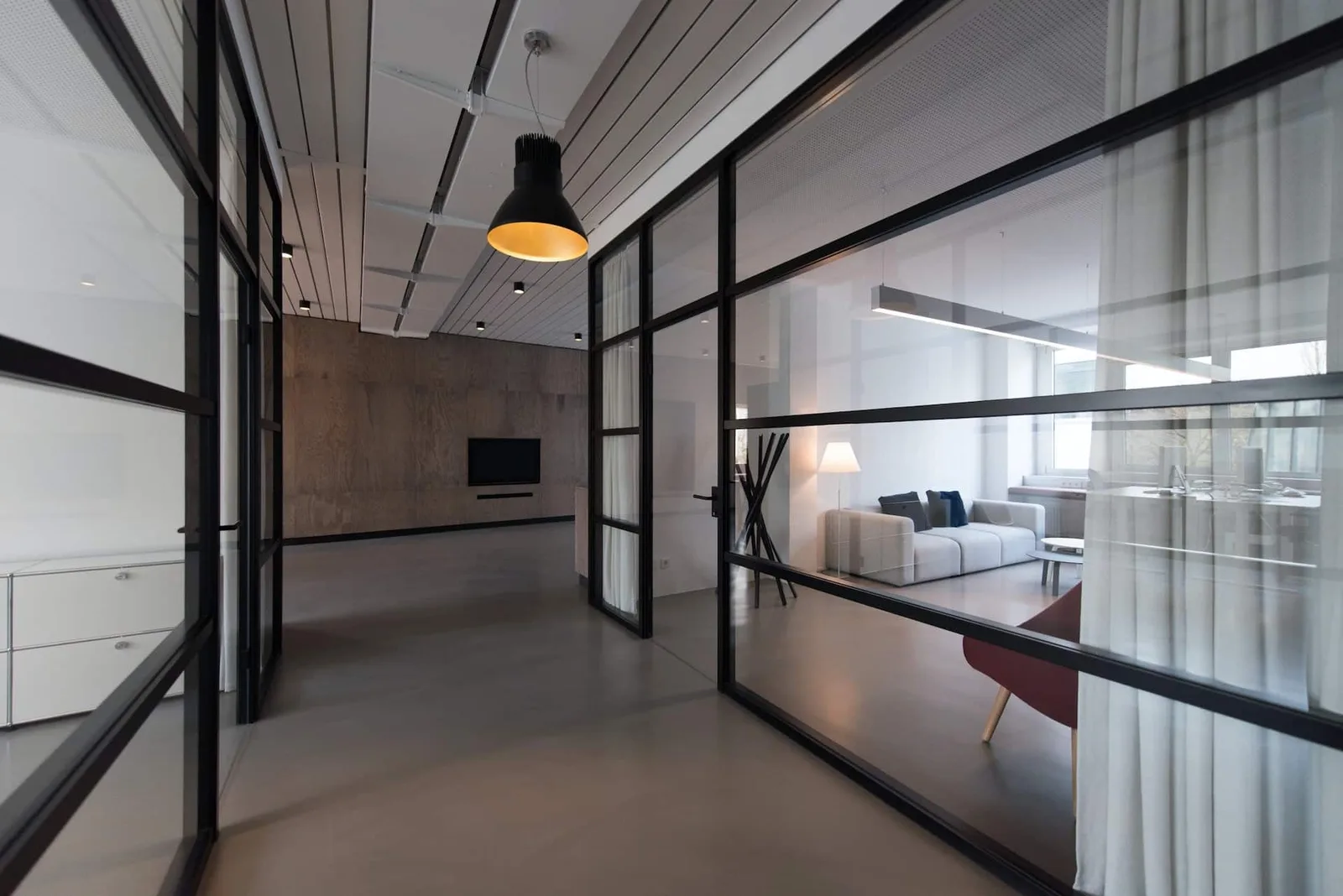 Intérieur lumineux séparé par une cloison amovible vitrée à structure noire entre un salon et un espace bureau.
