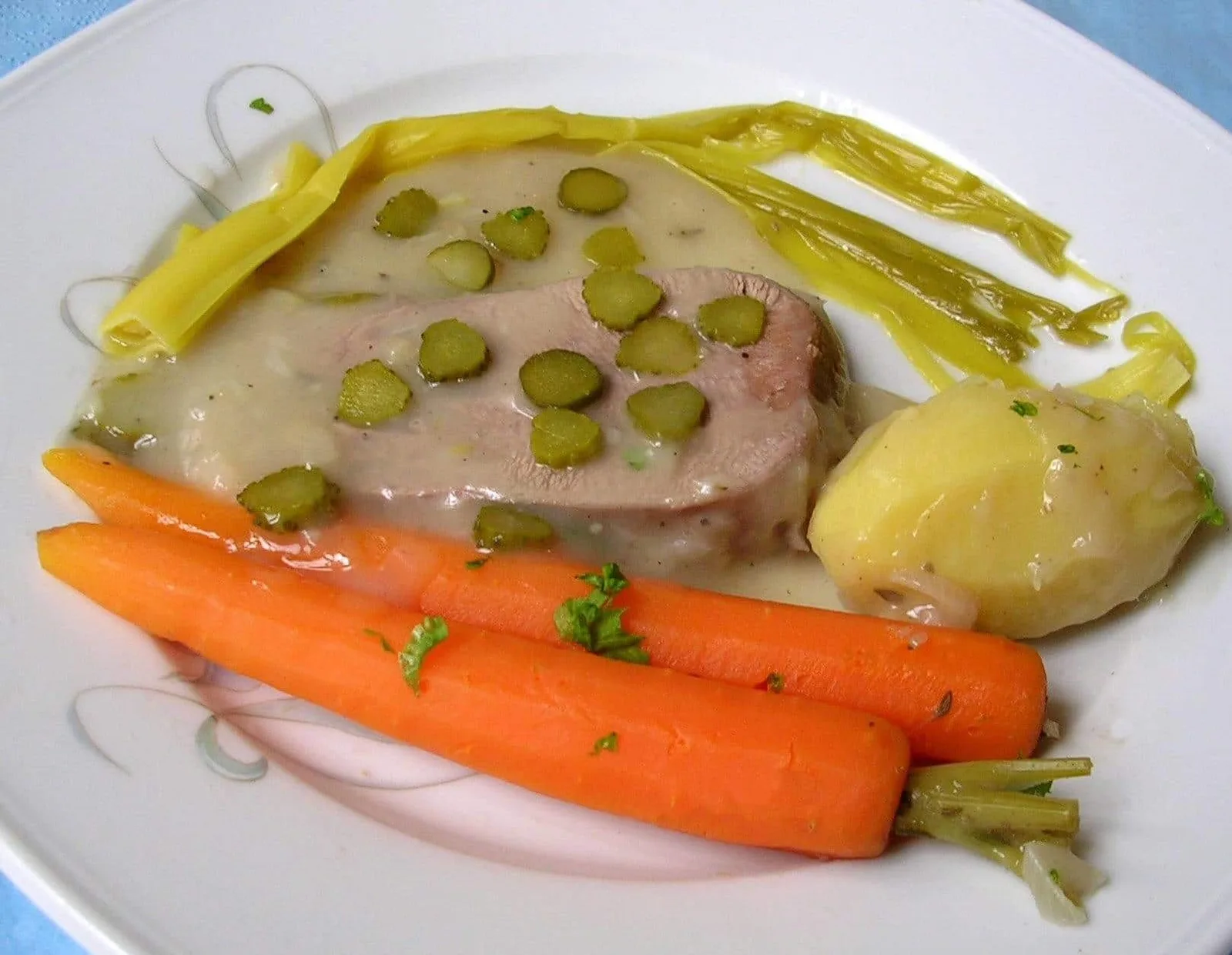 Langue de bœuf cuite et tranchée, servie avec une sauce piquante, des pommes de terre et des légumes du bouillon.