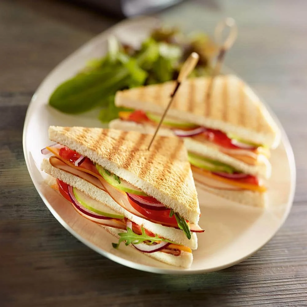 Club sandwich maison coupé en triangles, garni de poulet, salade, tomate et bacon, servi avec des frites.