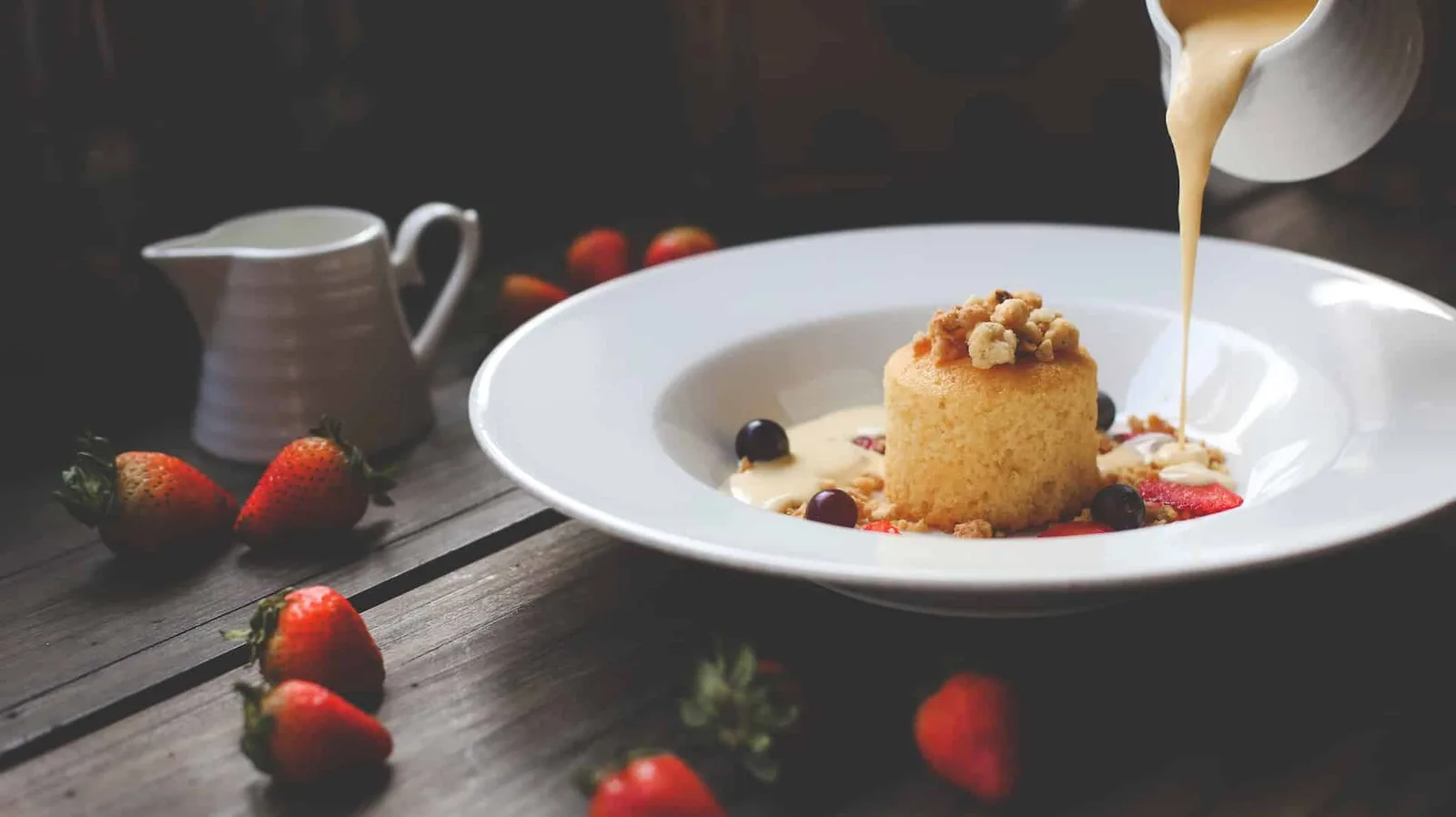 Sauce crémeuse à la vanille de Tahiti versée sur un dessert individuel, avec une gousse de vanille fendue à côté.