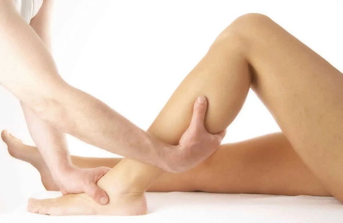 Femme assise sur son lit étirant doucement son mollet pour soulager une crampe nocturne.