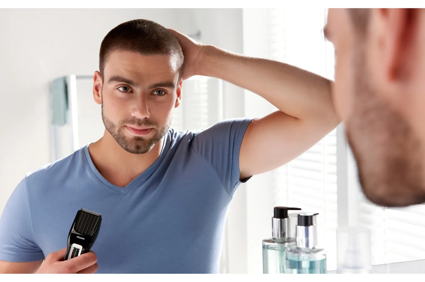 Personne tondant soigneusement les cheveux courts avec une tondeuse électrique et un sabot devant un miroir.