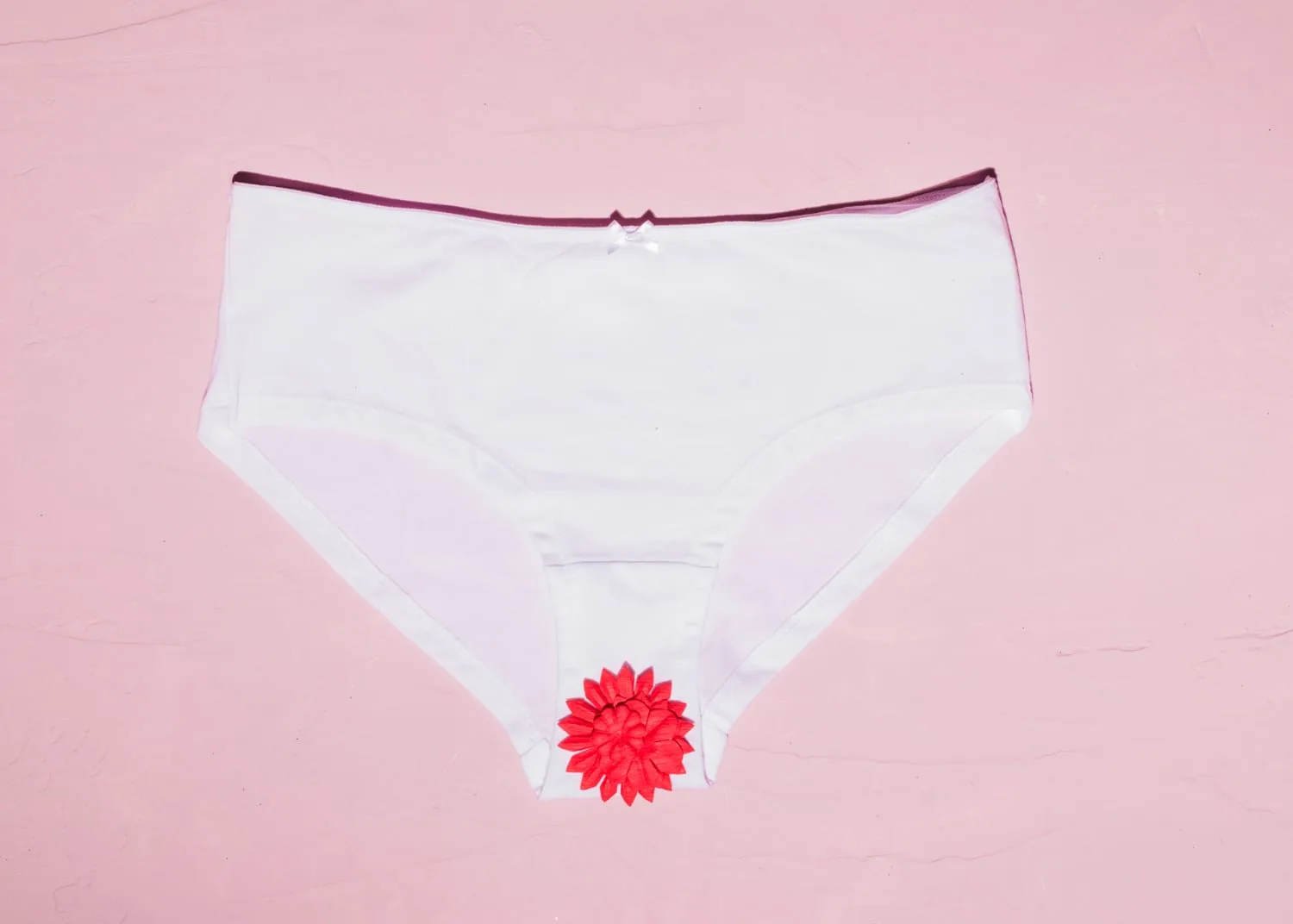 Culotte menstruelle lavable et paquet de serviettes hygiéniques posés sur un tissu clair, pour comparer les protections périodiques.