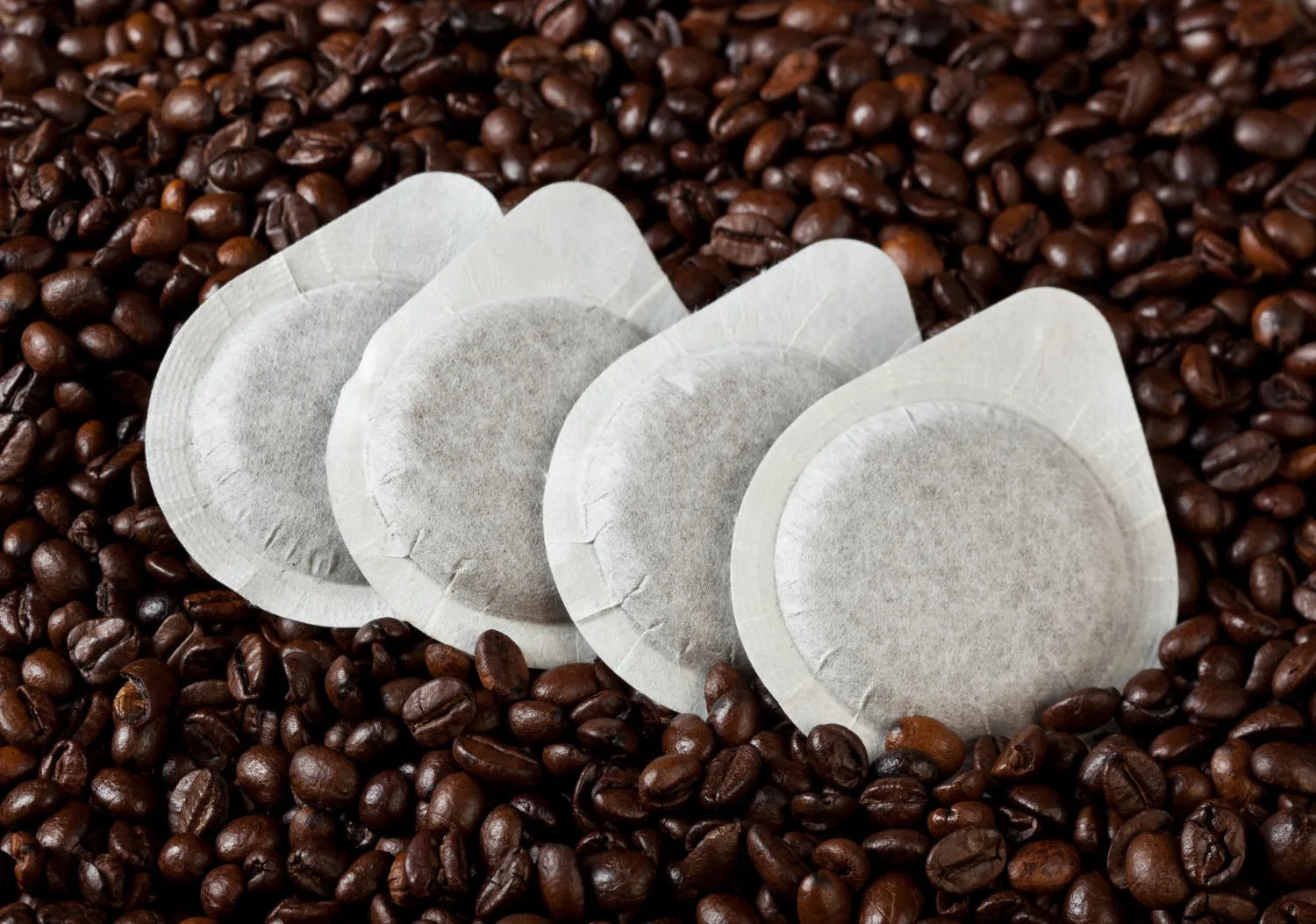 Tasse de café accompagnée de café en grains, d’une cafetière italienne et de dosettes Tassimo à recycler.