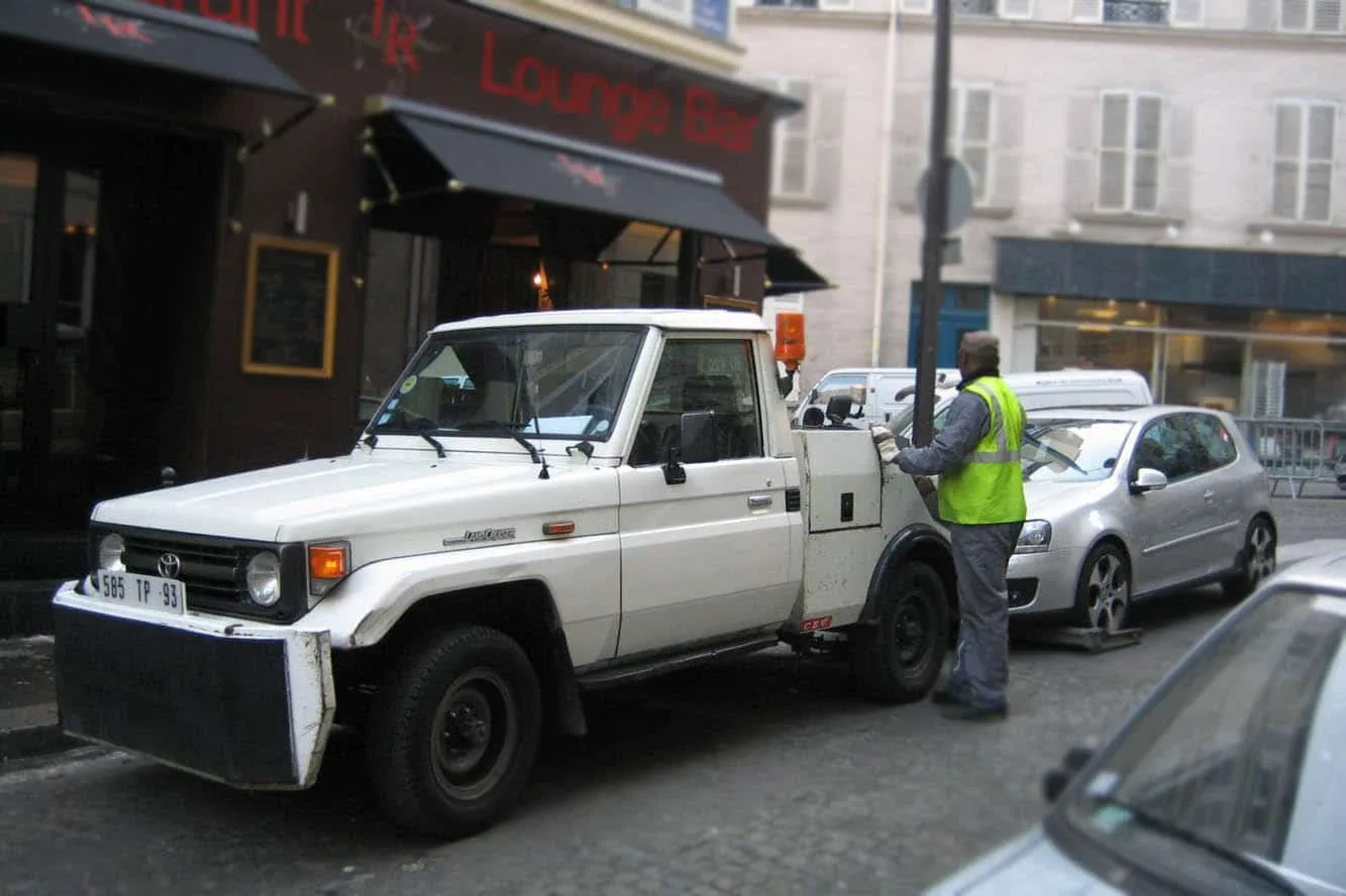 Conductrice devant une voiture emmenée par une dépanneuse de fourrière en ville.