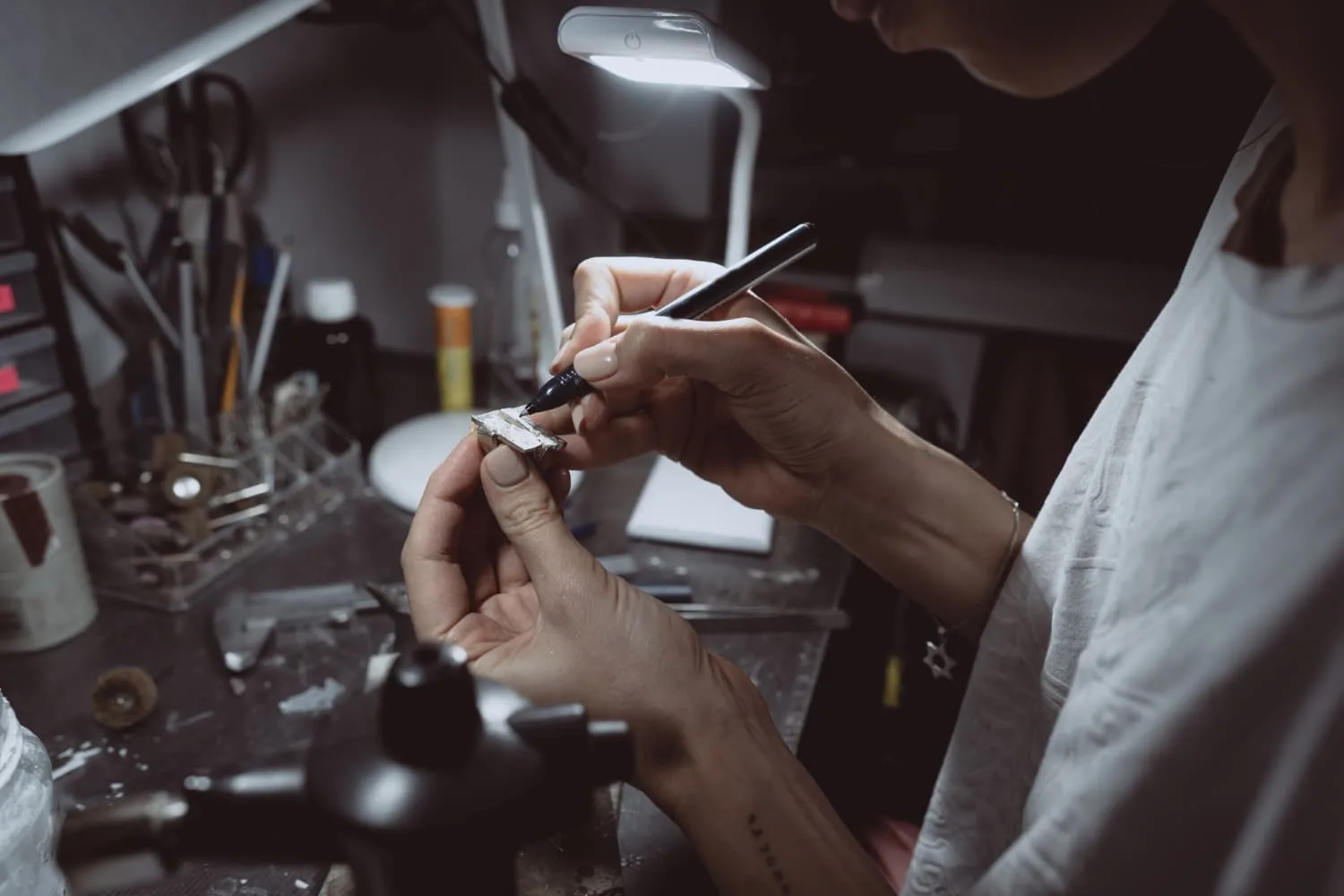 Mains façonnant un bracelet et des boucles d’oreilles en fil de laiton avec pinces de bijoutière sur un établi clair.