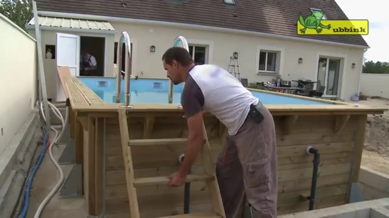 Piscine enterrée contemporaine dans un jardin paysager avec terrasse en bois et transats.