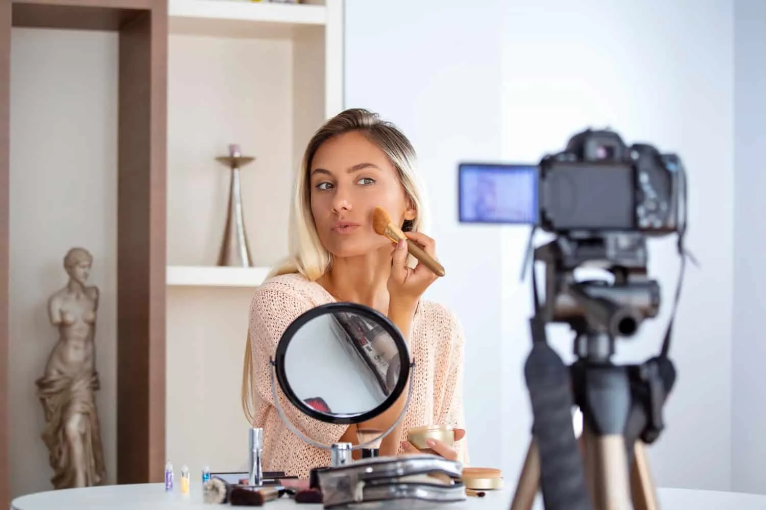 Sélection d'indispensables beauté comprenant des soins visage, du maquillage naturel, une brosse et des accessoires sur une coiffeuse lumineuse.