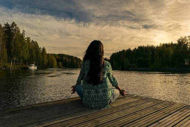 Femme assise confortablement chez elle, les yeux fermés, pratiquant une méditation de pleine conscience dans un intérieur lumineux.