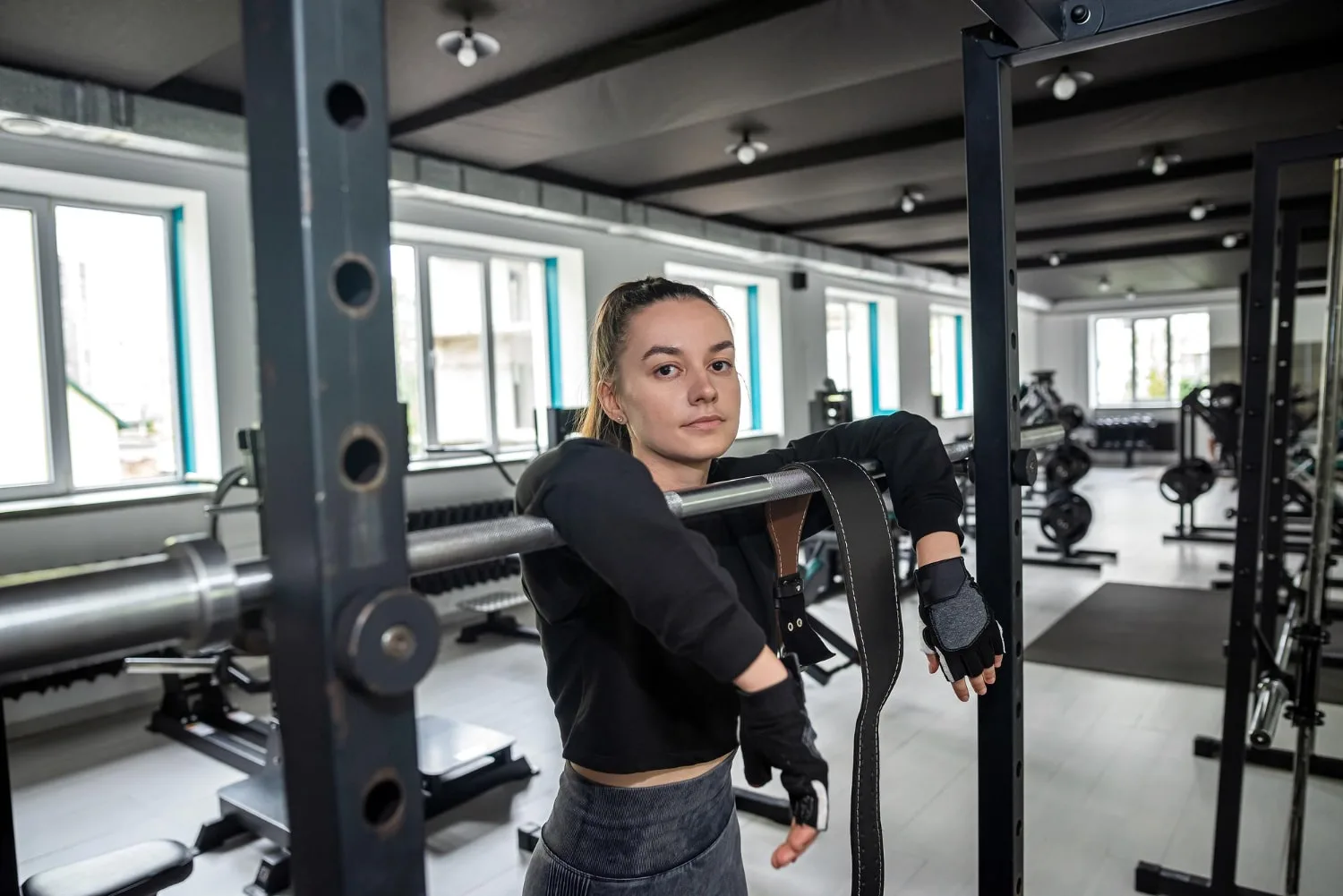 Femme débutante en musculation réalisant un squat avec haltère dans une salle lumineuse, accompagnée par une coach.