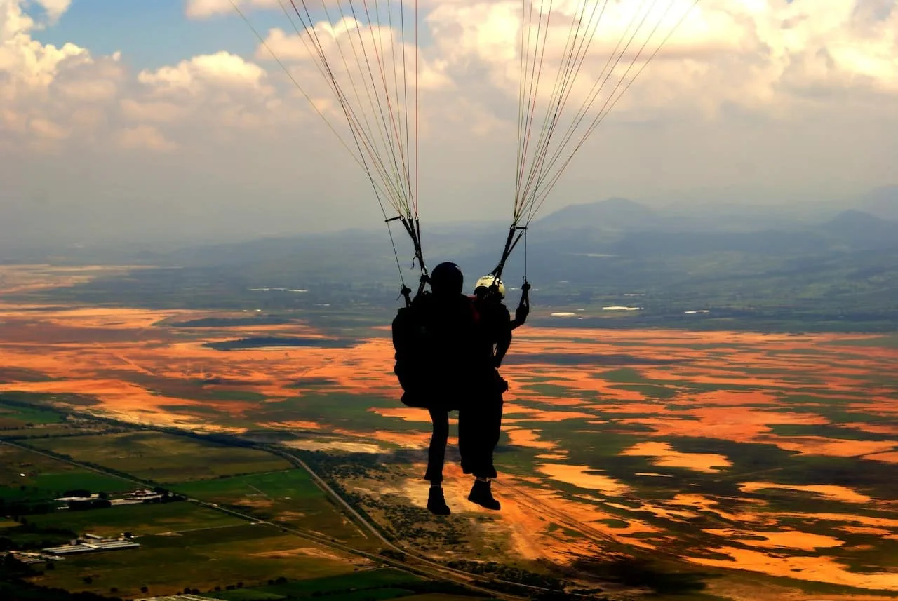 Une femme en tandem de parachute sourit dans le ciel, accompagnée de son moniteur au-dessus d’un paysage français.