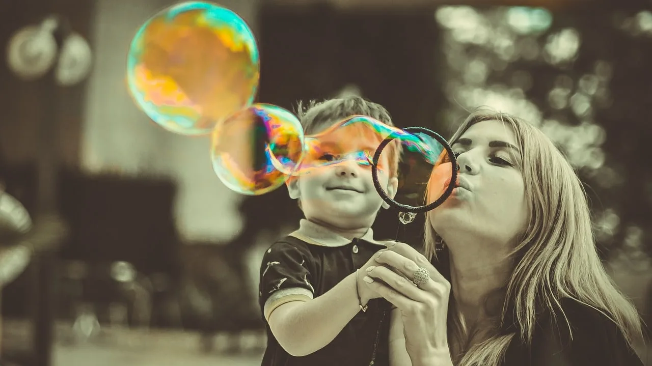 Une maman sourit et échange avec son bébé assis sur ses genoux en lui montrant un livre illustré.