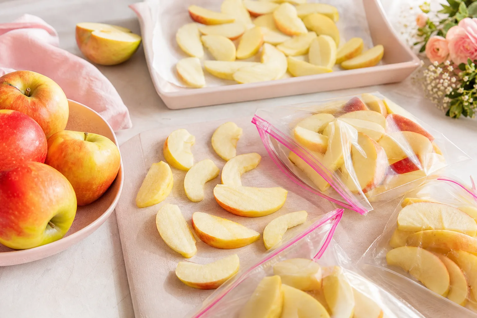 Quartiers de pommes préparés sur une plaque avant congélation, avec citron et sachets de conservation.